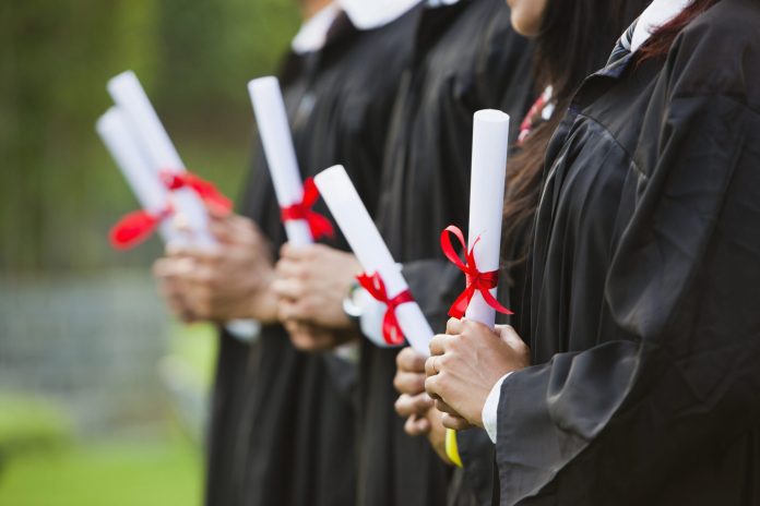 Students in graduation gowns holding diplomas