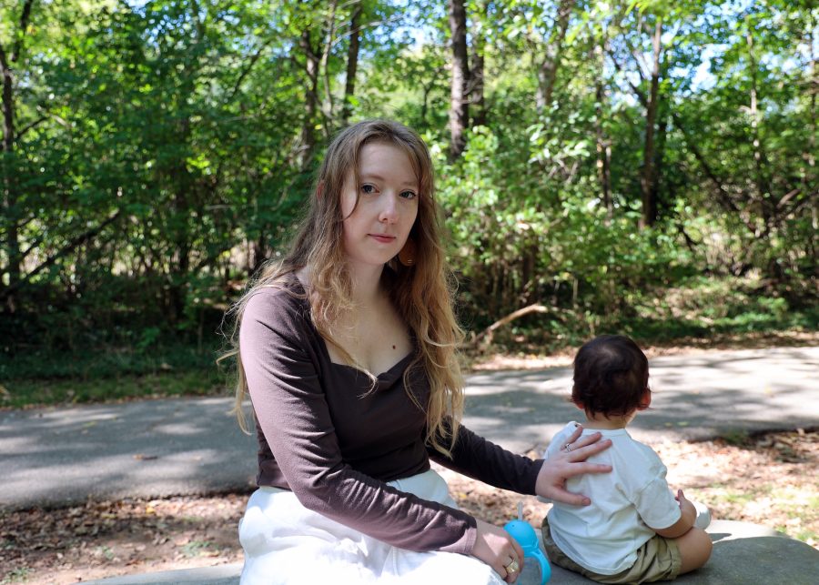 Madie Perez rests a hand on her young son beside a stone bench.