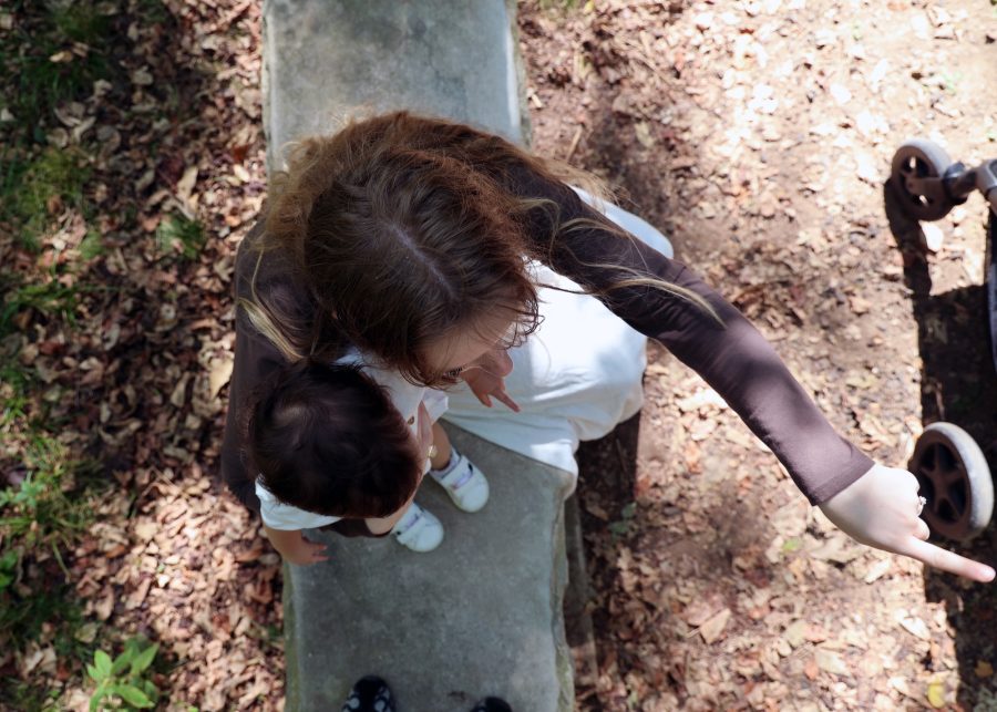 Madie Perez points down a park path while holding her young son.