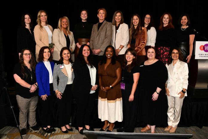 Group of women posing at an Iowa Women’s Foundation event, with the organization's logo visible on the podium.
