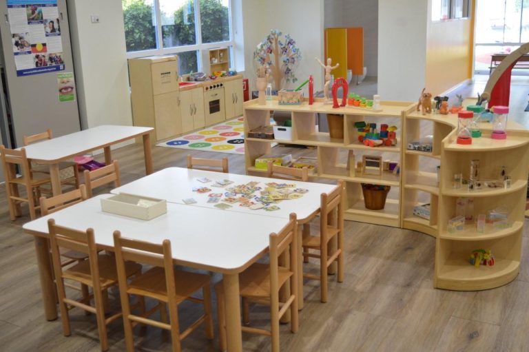 Child-sized wooden table and chairs with educational toys in a kindergarten classroom.