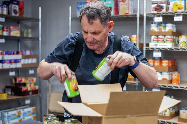 Volunteer wearing gloves placing canned food and essential supplies into a donation box.