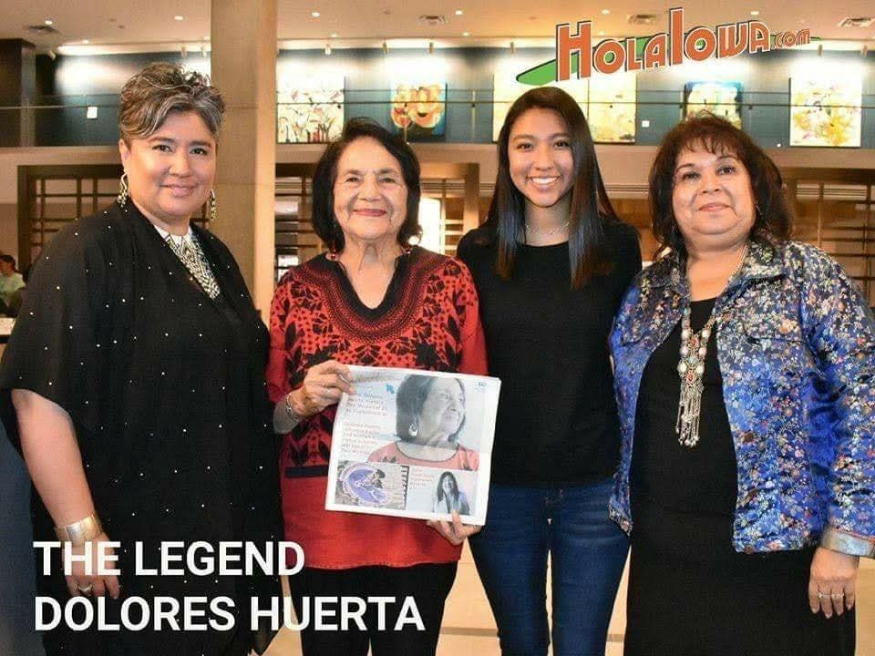 Dolores Huerta standing with three women at a community gathering, holding a printed publication.