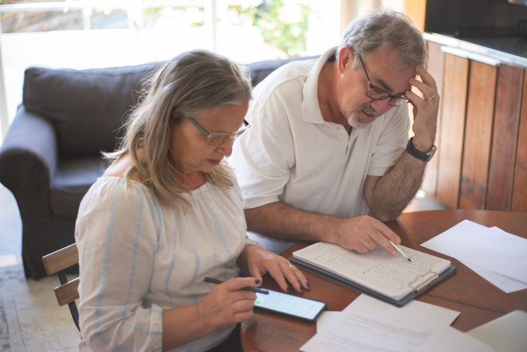 Older couple reviewing financial documents and a smartphone at home