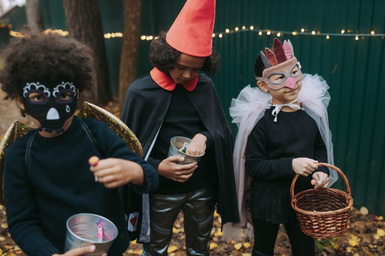 Children dressed in Halloween costumes collecting candy outdoors.